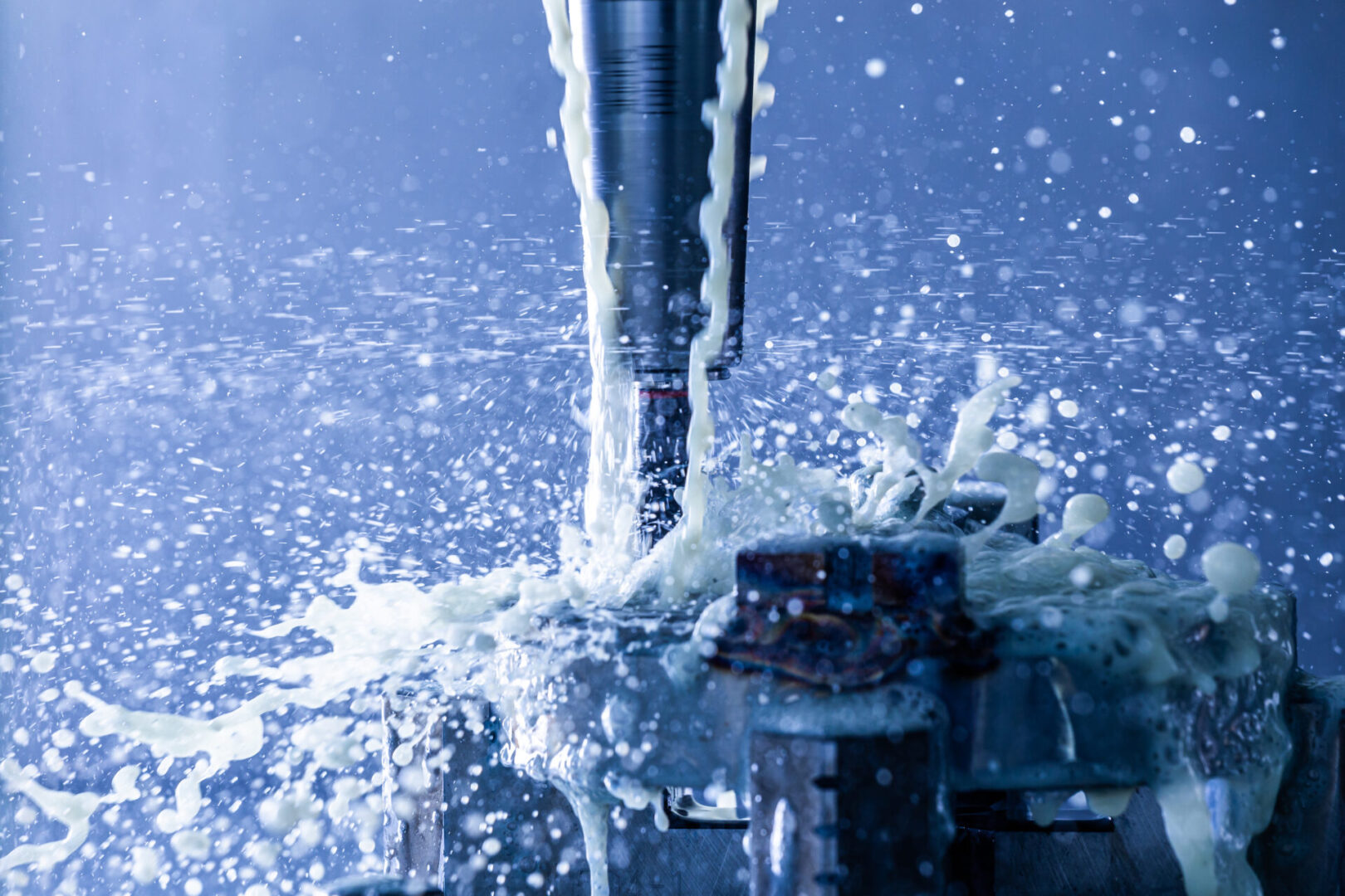 Abstract process of vertical cnc steel milling in slim hydraulic clamping chuck with external water coolant streams and splashes, close-up with blue tone, selective focus and background blur. Fast shutter speed for motion freezing.